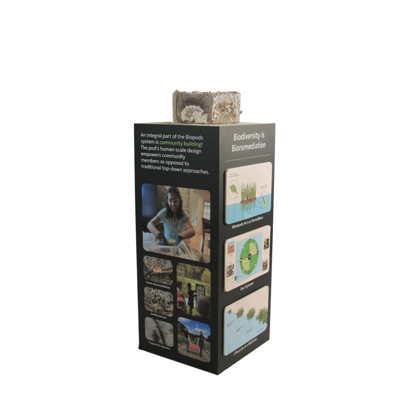 A rectangular display with images and text about biopods, emphasizing biodiversity and bioremediation. A block resembling soil or organic matter is on top