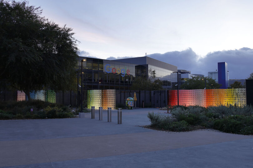 Google office building at dusk with colorful light installation in front and trees on the left.