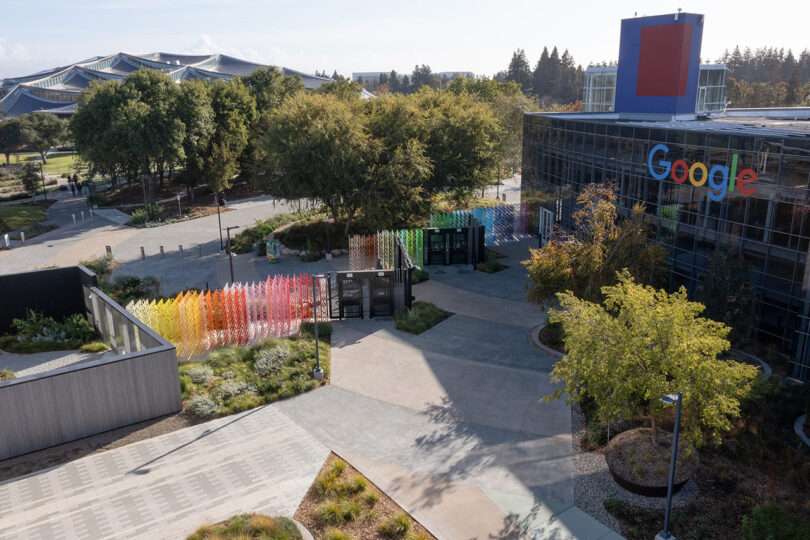 Google office exterior with colorful glass art installation, lush greenery, and modern architecture in a landscaped setting.