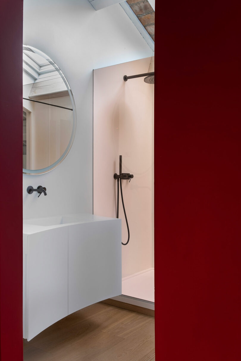 Bathroom with red walls, a round mirror above a white floating sink, and a walk-in shower with a rain showerhead and glass partition.