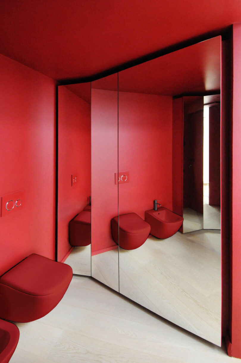 A red minimalist bathroom with two wall-mounted toilets and a large mirrored wall, reflecting the interior design.