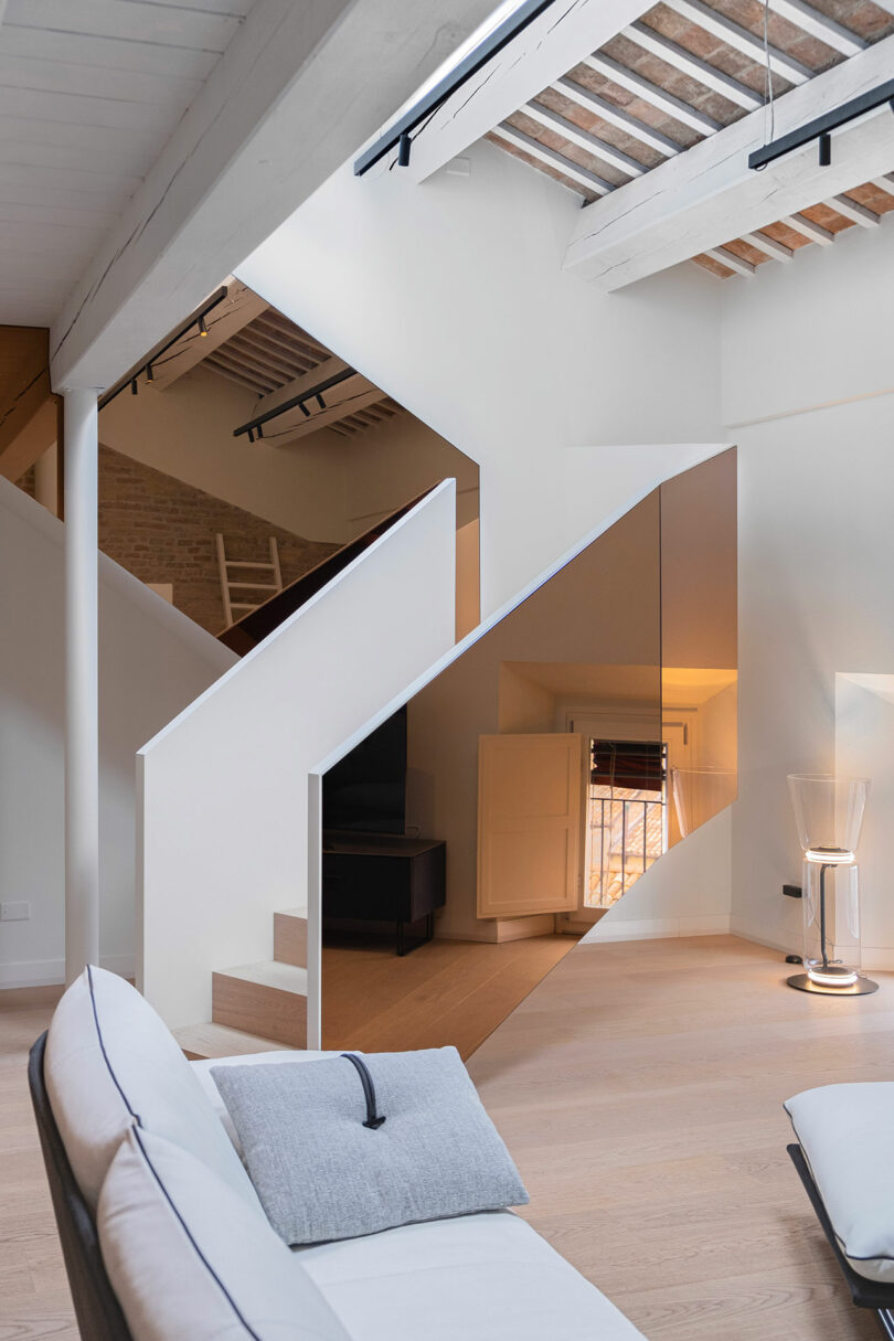 Modern interior with a white staircase, exposed wooden beams, a couch with cushions, and a minimalistic decor.