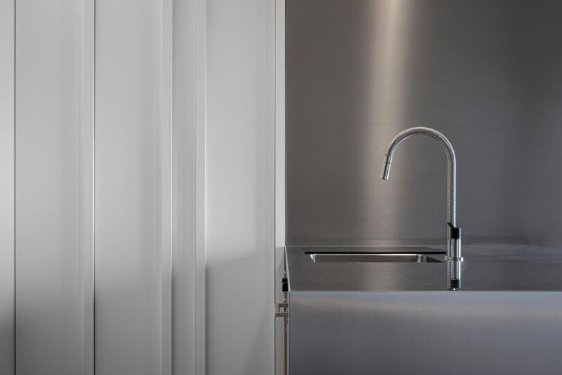 Minimalist kitchen with a metallic faucet and sink set against sleek white panel walls.