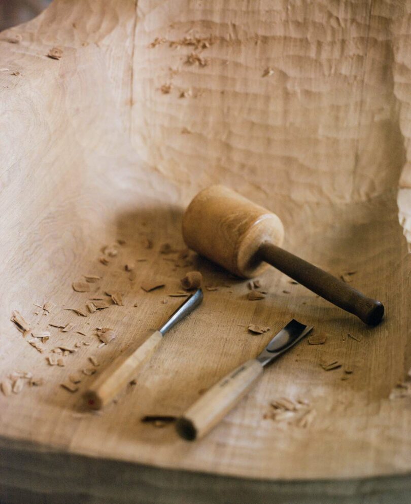 Wooden mallet and carving tools on a partially carved wooden surface with wood shavings scattered around