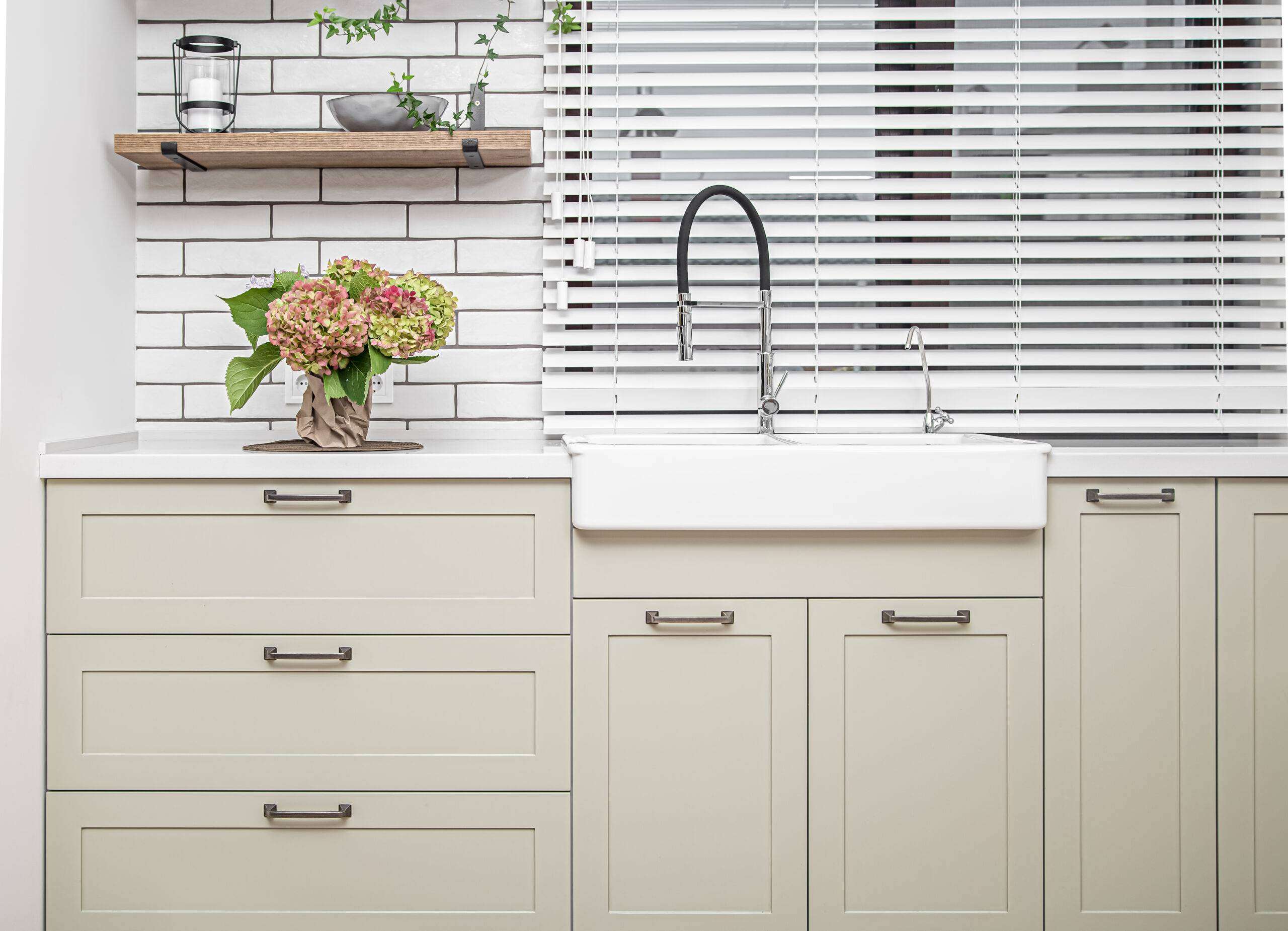 Kitchen interior with white kitchen cabinets with metal handles with a bouquet of flowers on the table.