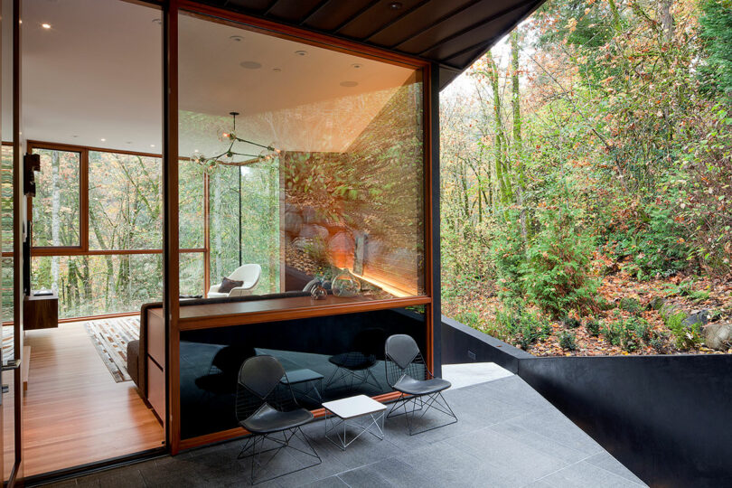 Modern glass-walled room with wooden accents and minimalist furniture, overlooking a lush forest view.