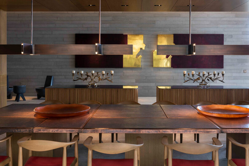 Dining room with a large wooden table, modern chairs, pendant lights, decorative candelabras, and abstract art on the wall.