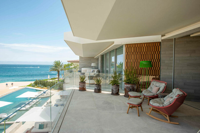 Luxurious beachfront balcony with cushioned chairs, potted plants, and a view of the ocean and pool.