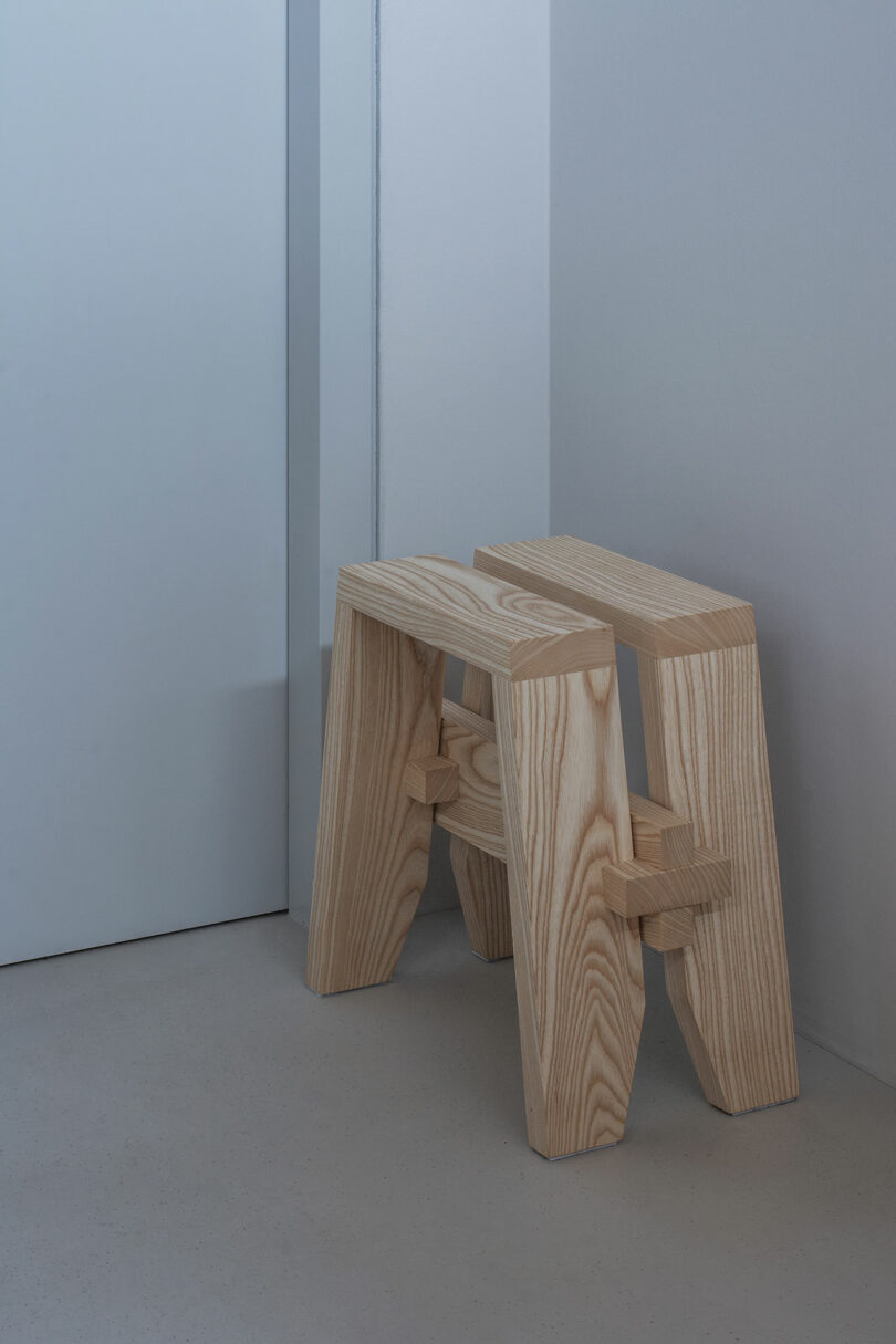 Wooden stool with a minimalist design placed against a light-colored wall indoors.