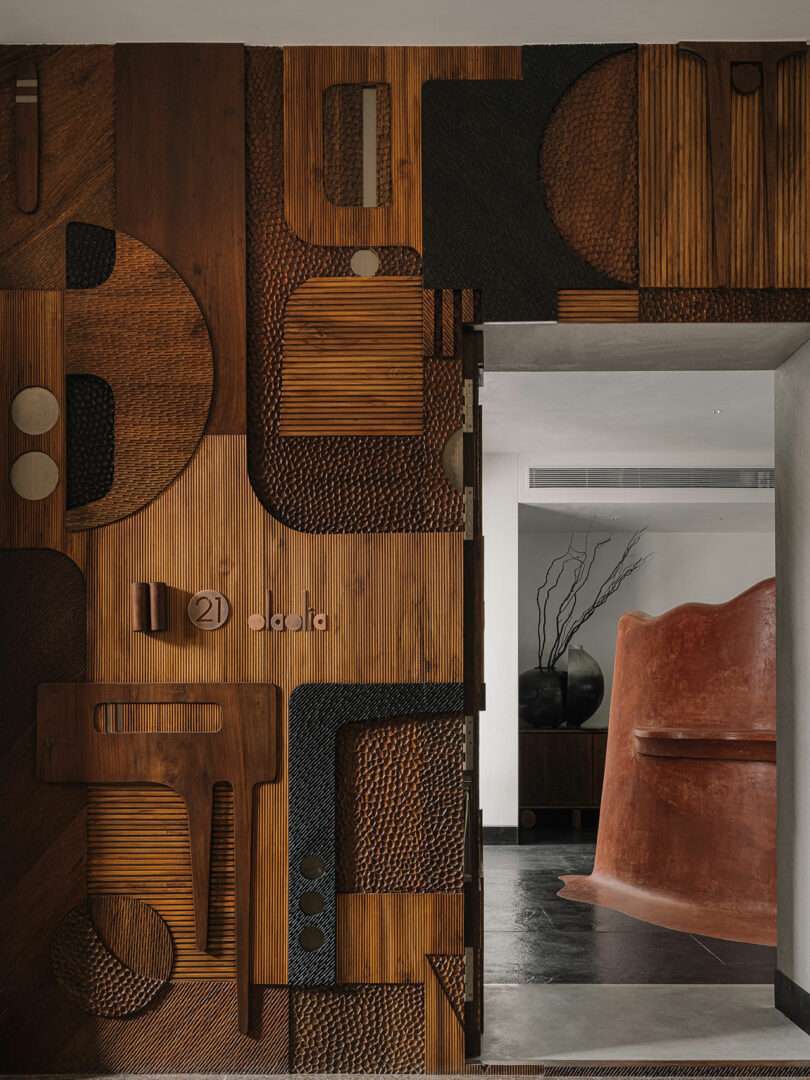 Intricate wooden wall art with geometric patterns beside an open doorway leads to a room by Studio Nishita Kamdar, showcasing a curved reddish-brown structure and dark flooring.