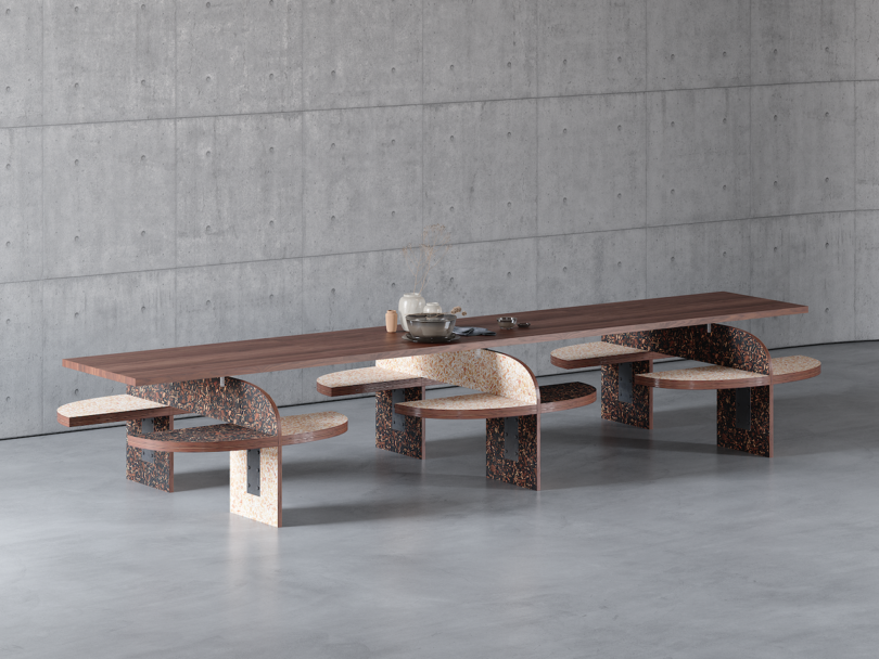 A modern dining table with a long wooden top and uniquely designed chairs featuring curved backs and stone-like textures, set in a minimalist concrete-walled room