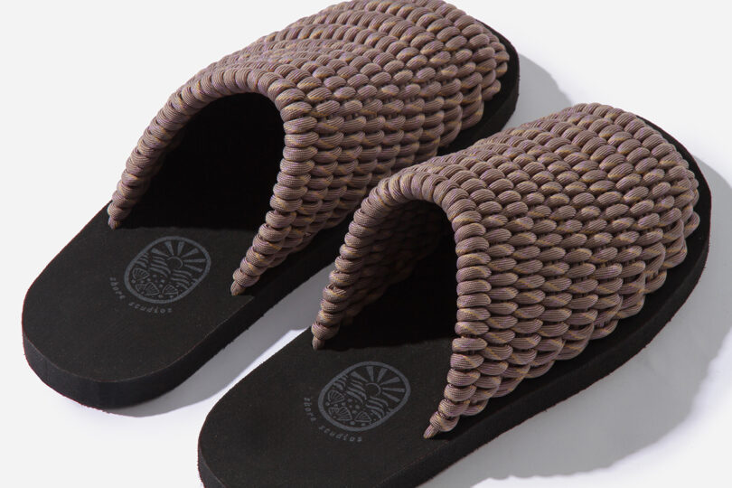 Pair of woven sandals with thick, textured straps and flat black soles on a white background.