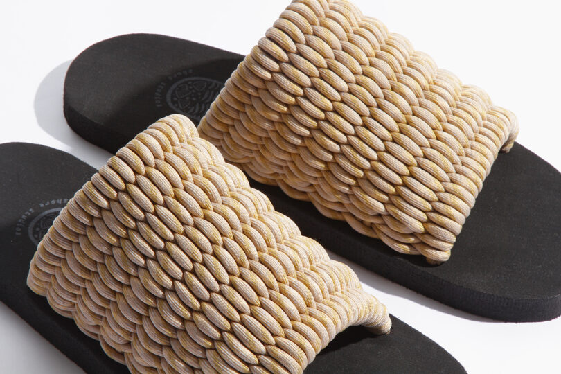 Pair of black sandals with thick, woven beige straps, displayed on a white background.