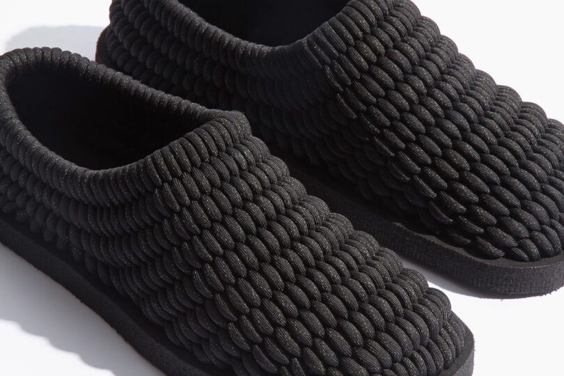 Black slippers with a textured, coiled rope design on the upper surface, set against a white background.