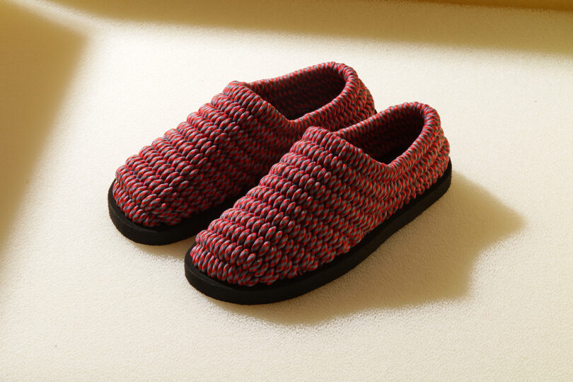 Pair of red and black woven slippers with black soles, resting on a light-colored surface.