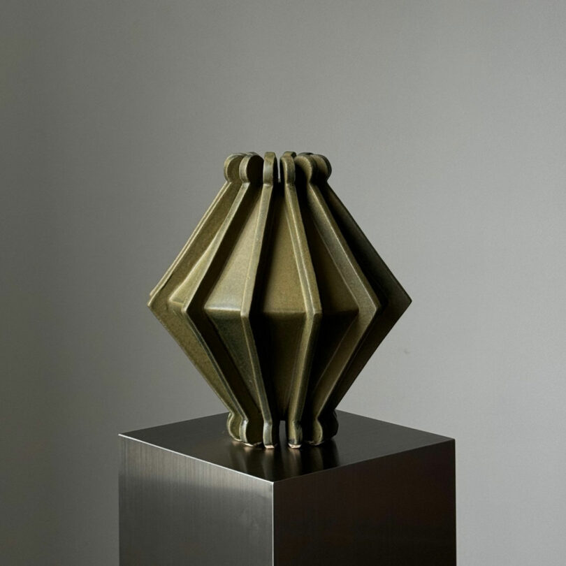 Geometric sculpture with an accordion-like design on a metallic pedestal against a plain background.