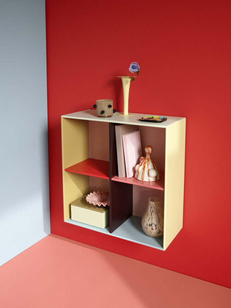 Wall-mounted shelf with assorted decorative items, books, and vases against a red and blue wall.
