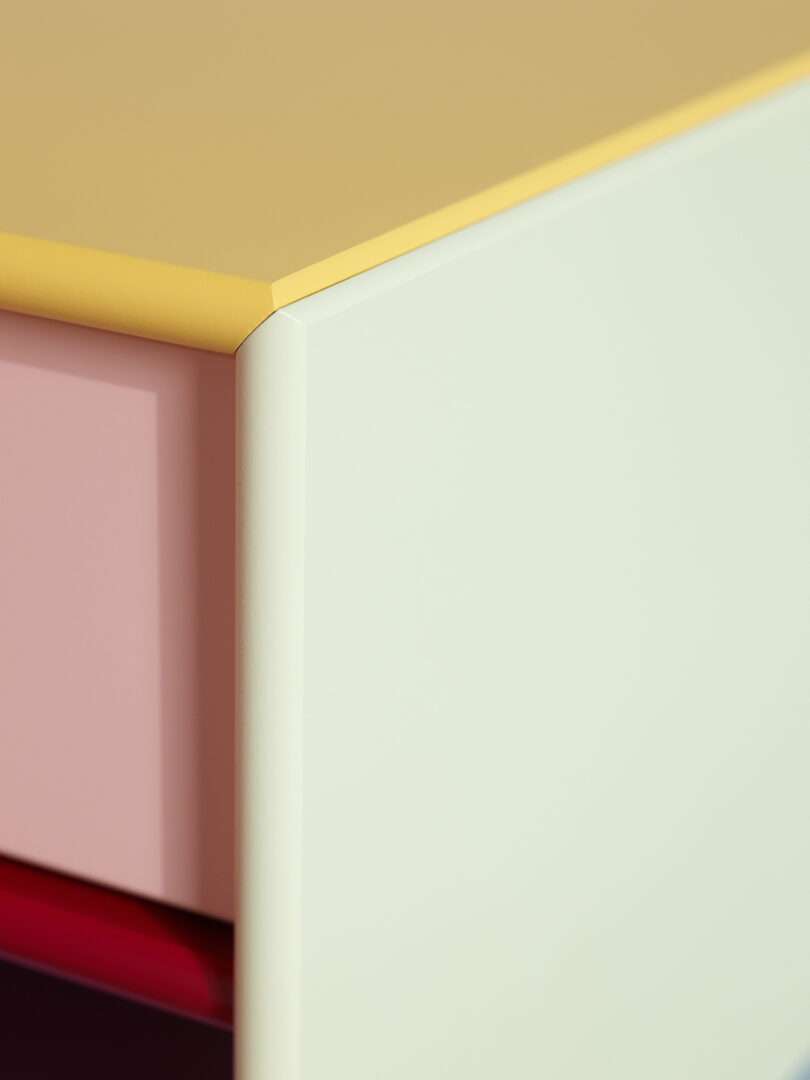 Close-up of a modern cabinet corner with a yellow top, pale pink side, and a light green front.