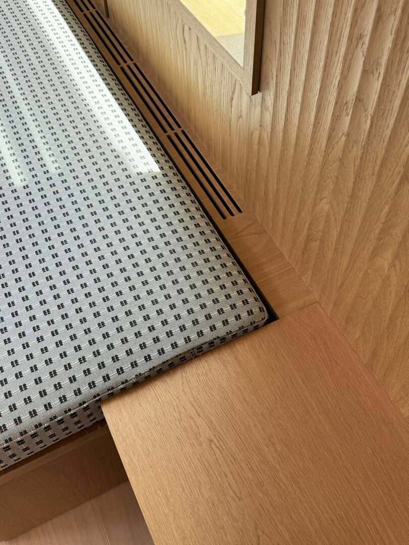 A corner of a wooden bench in the Shift House features a patterned cushion with a vent seamlessly integrated into the wood paneling.