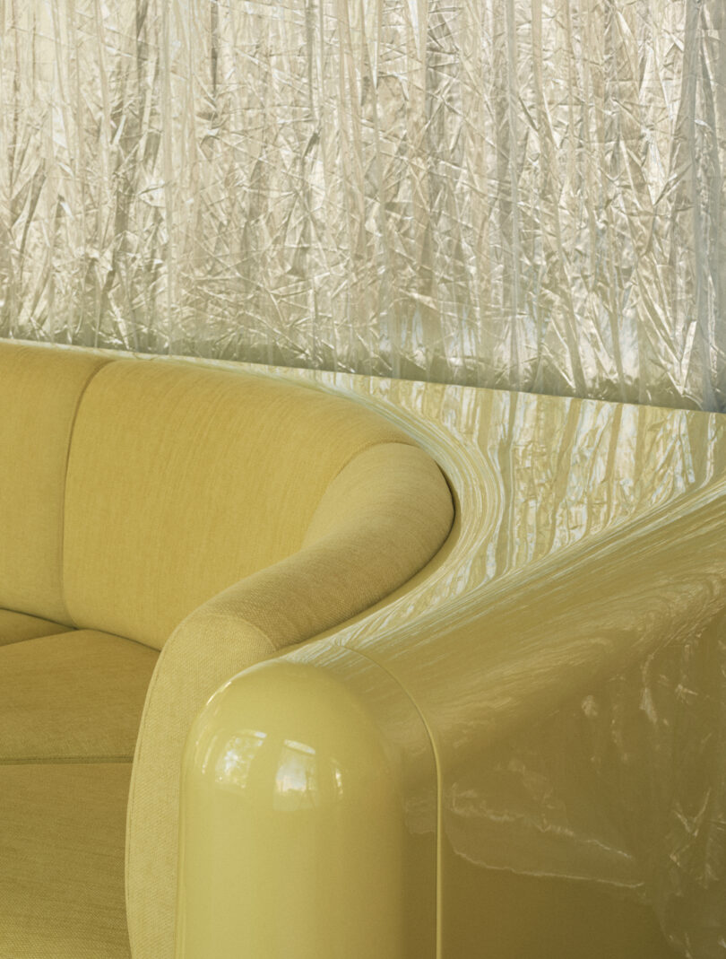Yellow curved sofa with glossy armrest in front of a crinkled, shiny gold curtain
