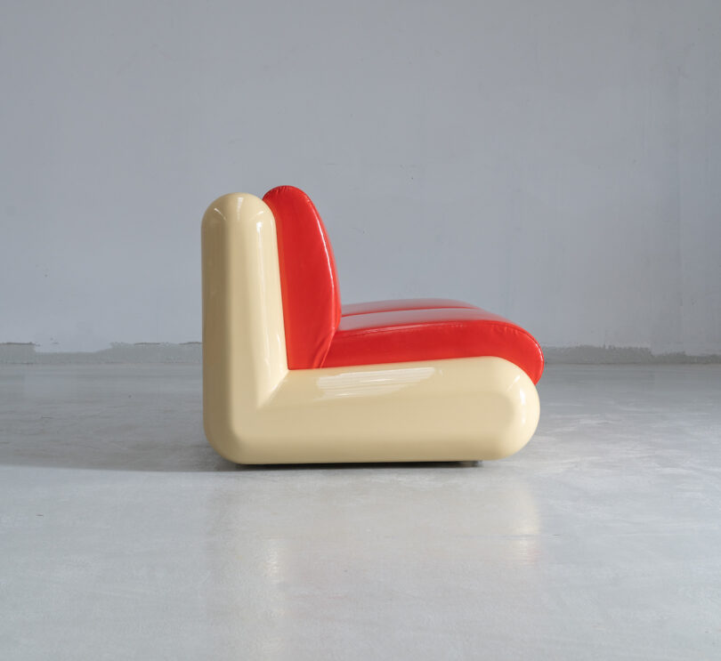 A modern chair with a glossy red seat and beige L-shaped frame against a plain gray background