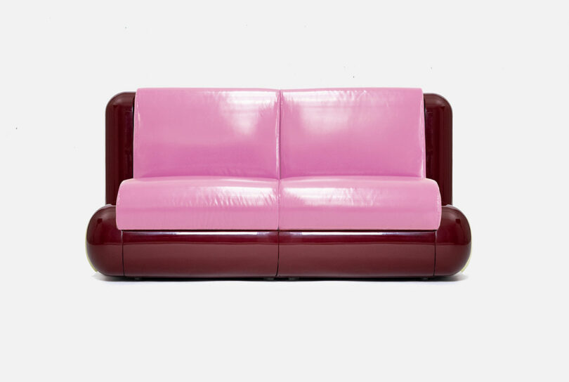 A modern sofa with glossy pink cushions and dark maroon rounded armrests and base, set against a plain white background.