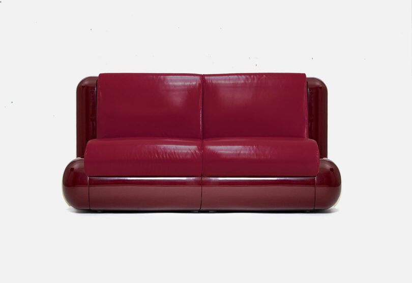A modern, glossy red leather sofa with rounded edges and minimalist design, set against a plain white background.