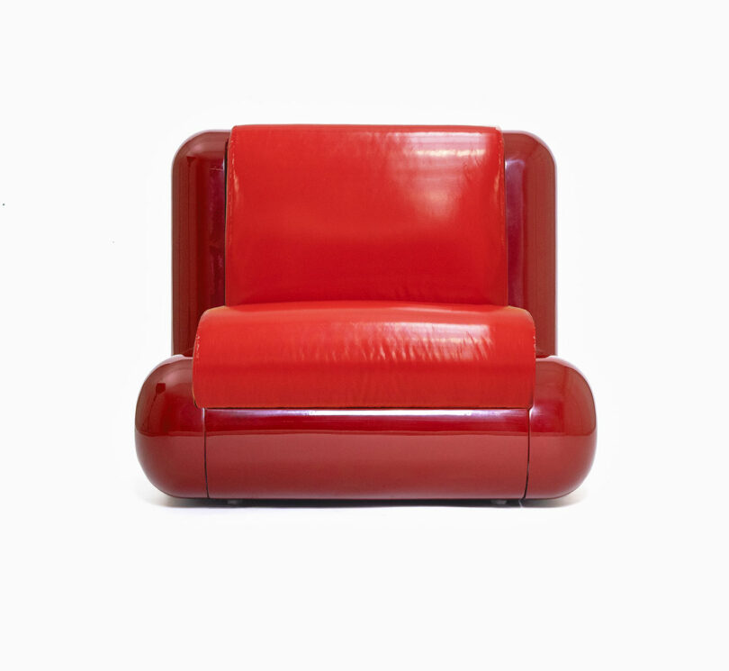 A modern, glossy red loveseat with rounded edges and a smooth leather-like finish set against a plain white background.
