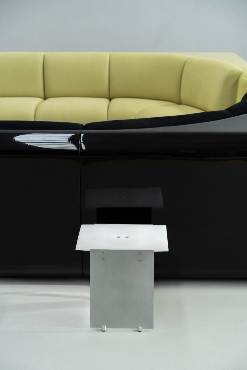 A modern room with a curved black and yellow couch and a minimalist metal side table with a white square top