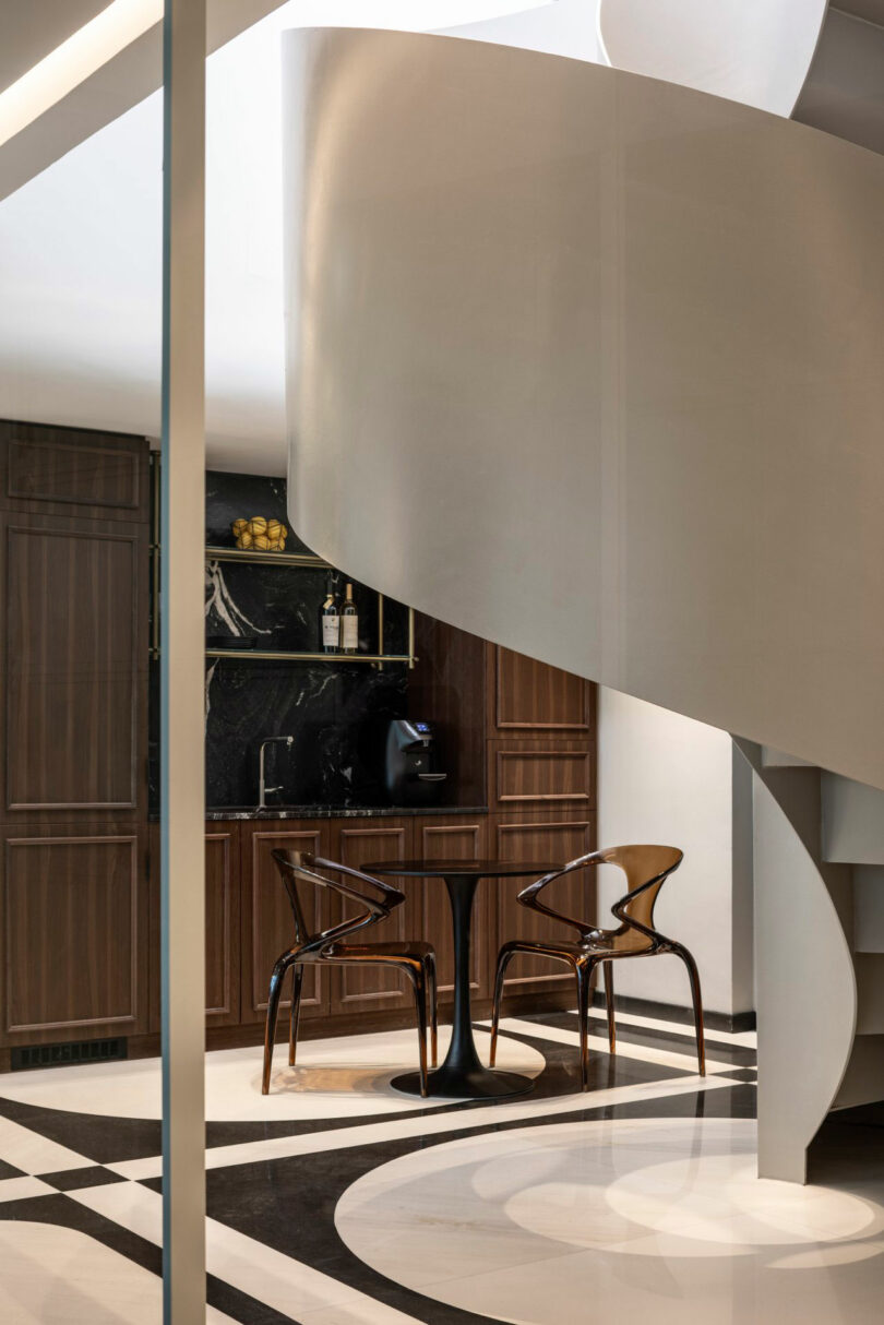 A modern kitchen with dark wood cabinets, black backsplash, a small round table with two chairs, and a white spiral staircase in the foreground.