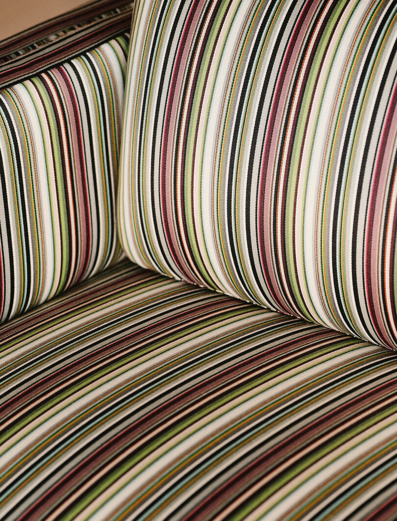 A close-up view of an upholstered chair with a striped fabric pattern in shades of green, brown, black, and white.