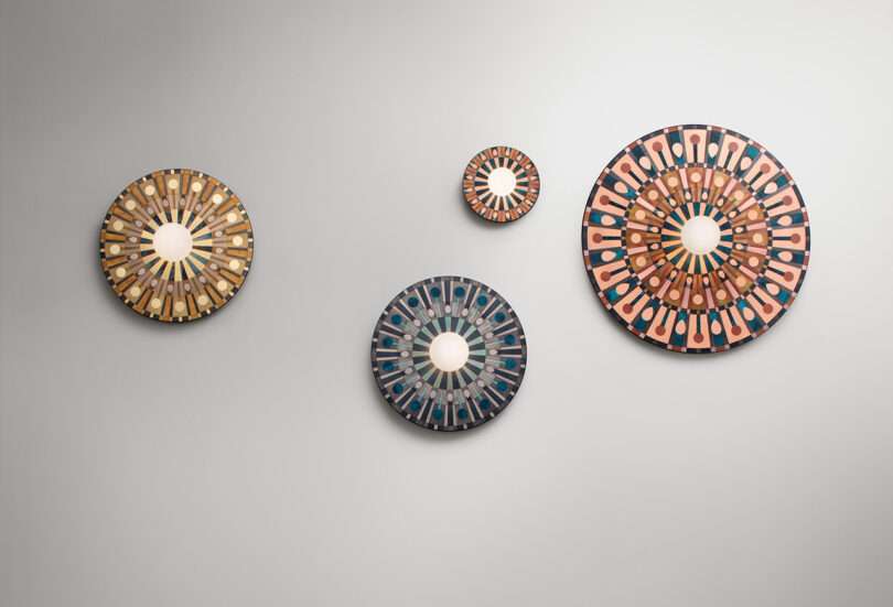 Four round, decorative wall mirrors arranged in a pattern on a plain white wall. Each mirror features intricate, colorful designs with a central reflective surface.