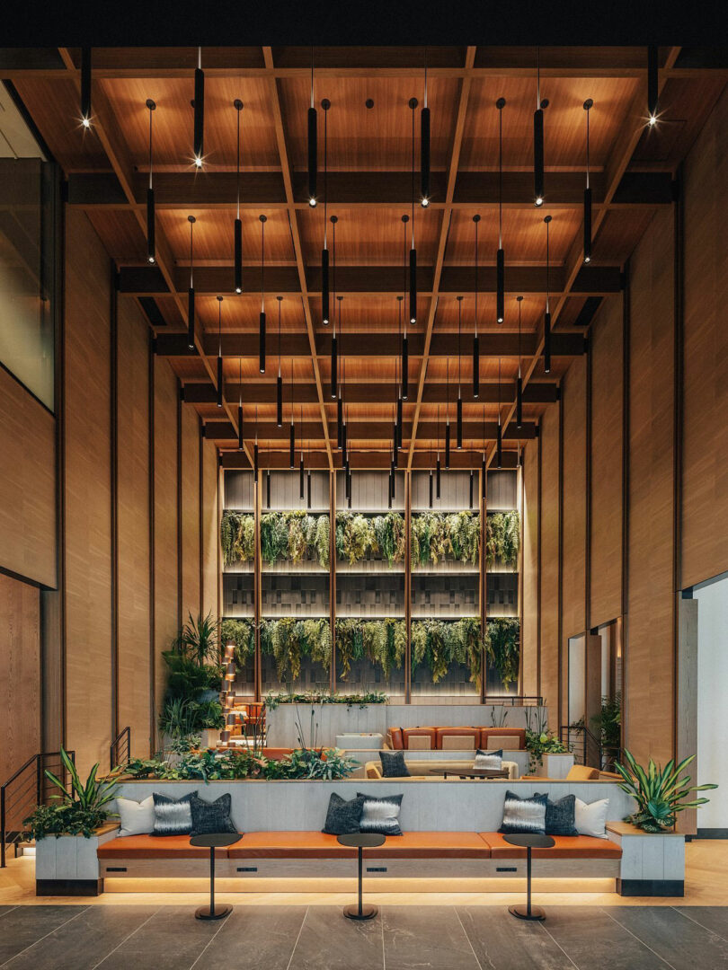 Modern lobby with wooden ceiling, a vertical garden wall, contemporary seating, and soft lighting, featuring plants and neutral-toned cushions inspired by JUN AIZAKI's innovative design ethos.