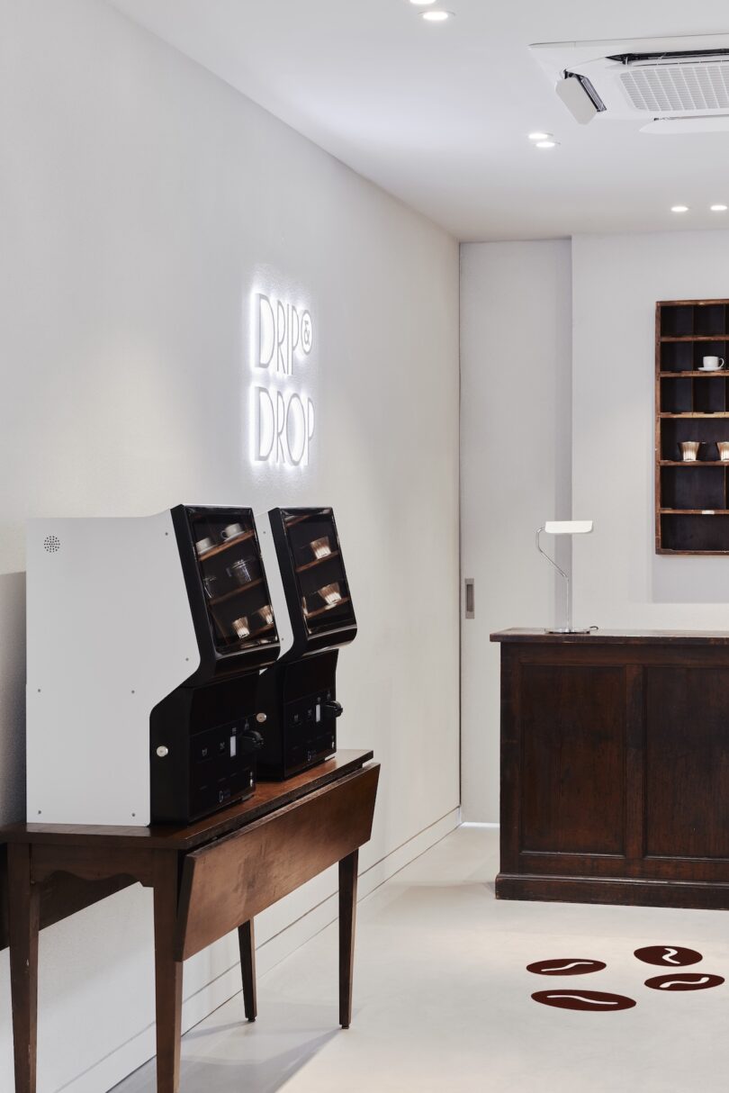 A minimalist coffee shop theme interior at HOTEL DRIP&DROP with two coffee machines on a wooden table to the left, a neon sign reading
