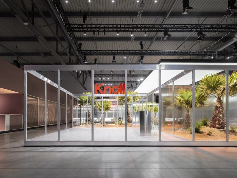 A modern glass-walled pavilion displays desert plants inside an industrial exhibition hall, with 