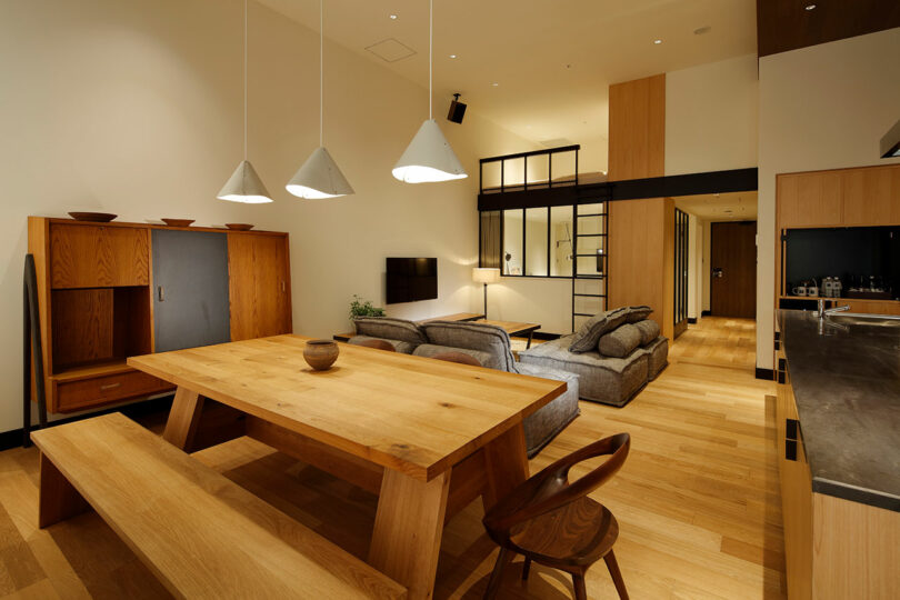 Modern open-plan living and dining area with wooden furniture and gray sofas, pendant lights and minimalist decor