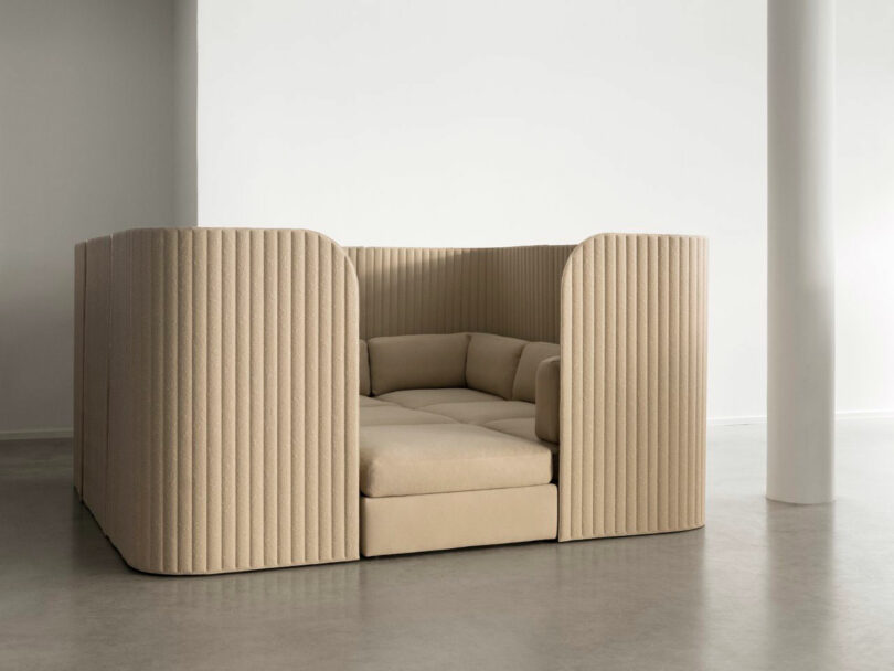 A beige, upholstered seating pod with high, ribbed walls forming a private, enclosed lounge area in a minimal, light-filled room.