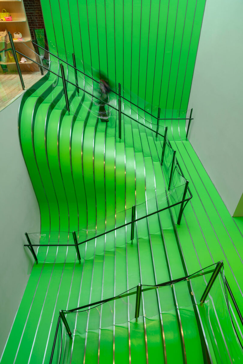 A bright green staircase with wavy, undulating lines and glass railings spans several floors in a modern interior space.