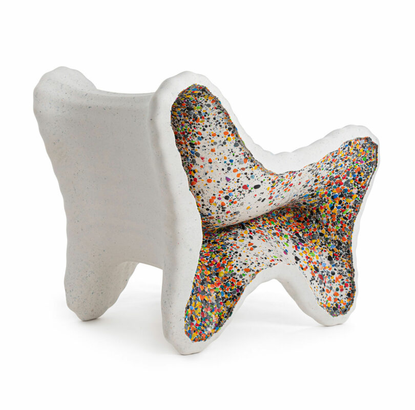 White sculptural chair with an abstract shape, inspired by In-Side Thomas Heatherwick, featuring a colorful, speckled interior surface with multicolored dots.