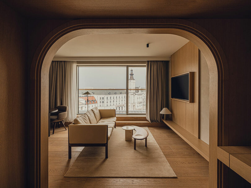 A modern living room with wood accents, neutral furniture, and a large window offering a city view featuring a clock tower.