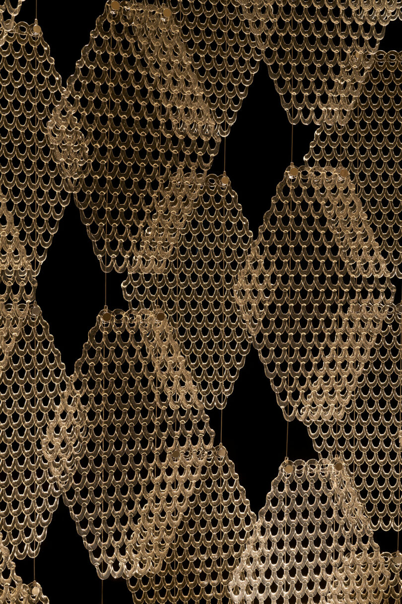 Gold geometric pattern made of interlocking circular rings forms diamond shapes against a black background, reminiscent of motifs found beneath The Great Tree.