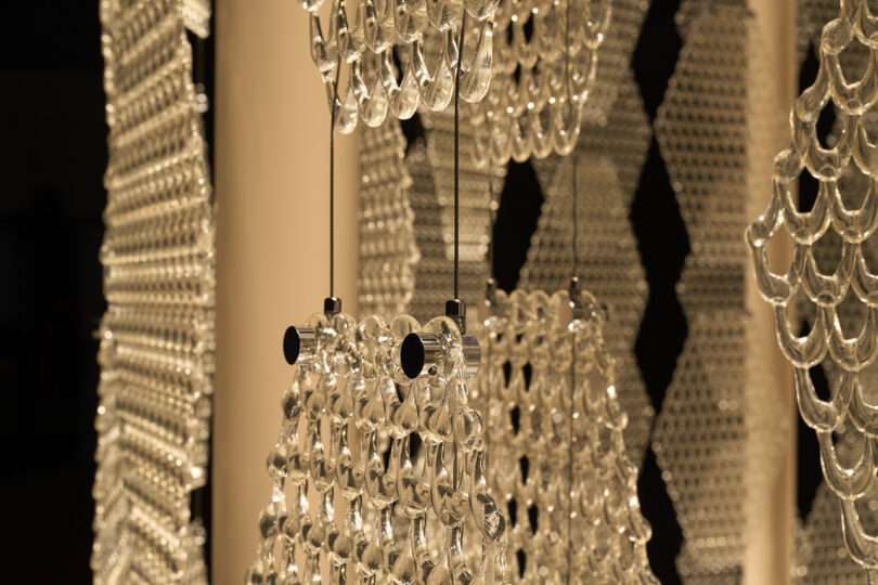 Close-up view of hanging glass or crystal light fixtures with a geometric pattern, illuminated by warm lighting—reminiscent of ornaments beneath The Great Tree.