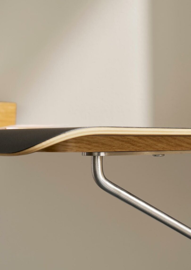 Close-up of a Carl Hansen & Son table designed by Anker Bak, featuring a wooden tabletop with a curved edge and a metal leg underneath, set against a neutral background with soft lighting