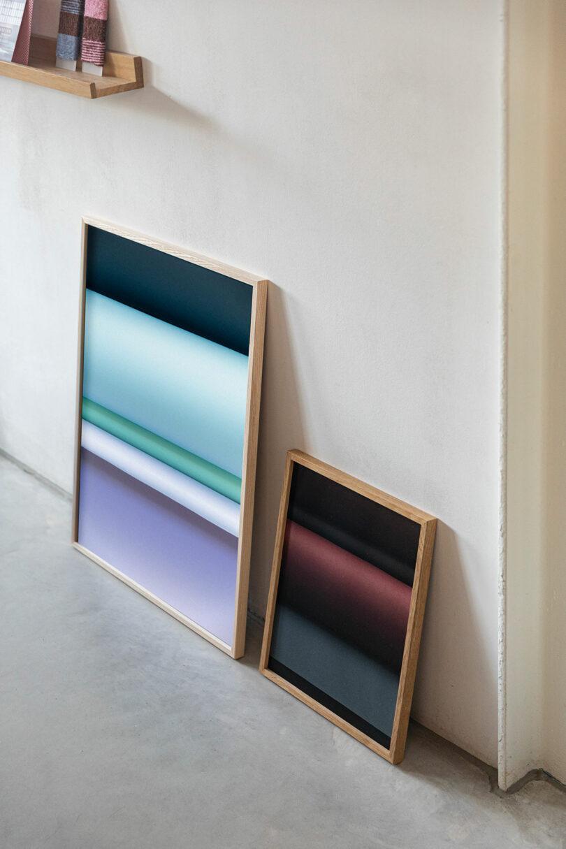 Two framed abstract gradient artworks, one large and one small, are leaning against a white wall on a concrete floor.