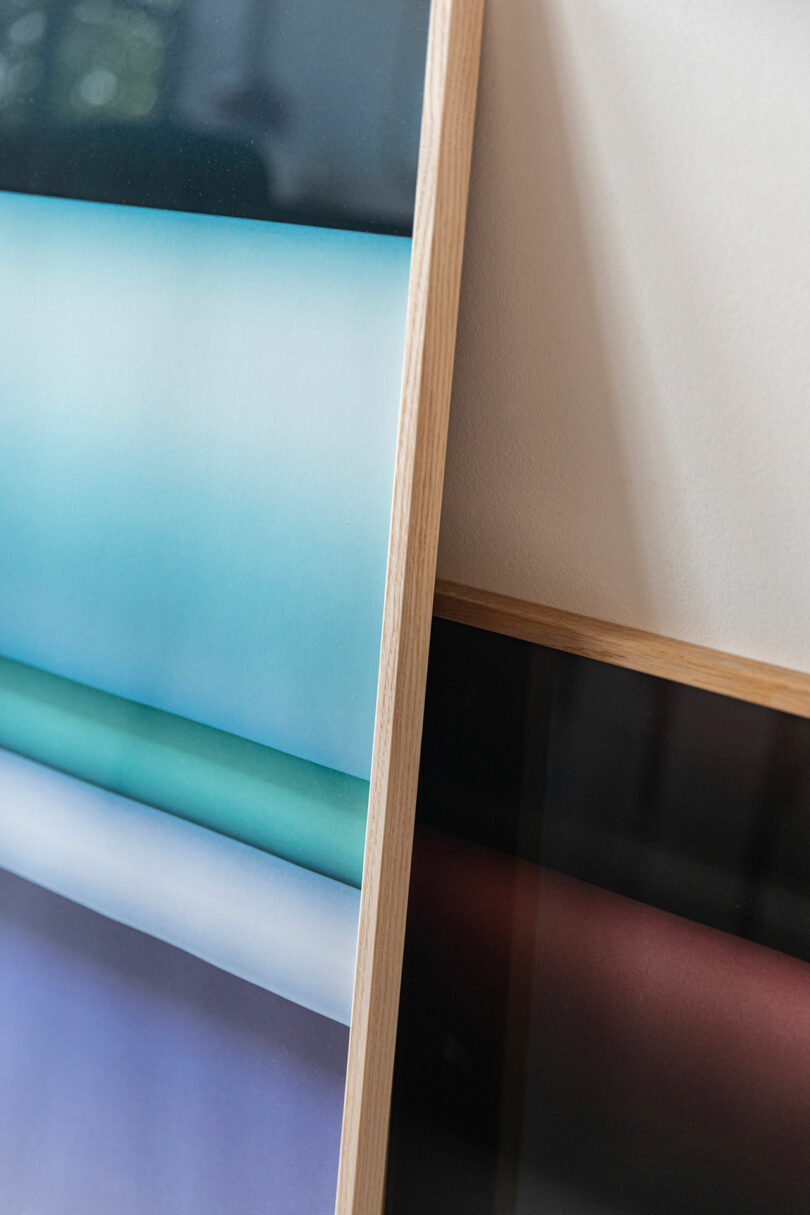 Two framed abstract prints with horizontal color gradients, one in blue and green tones, the other in dark red and black, leaning against a white wall.