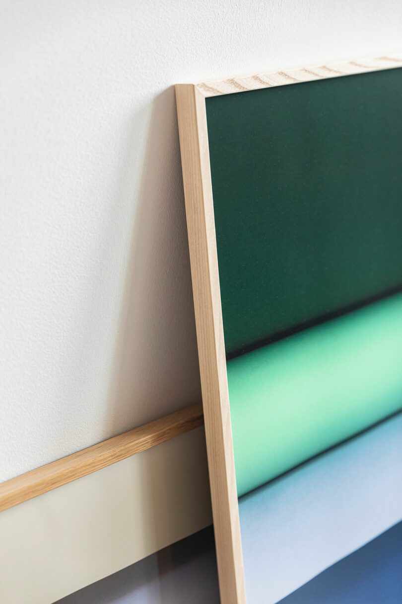 Two framed abstract prints with wooden frames are leaning against a white wall, one overlapping the other.