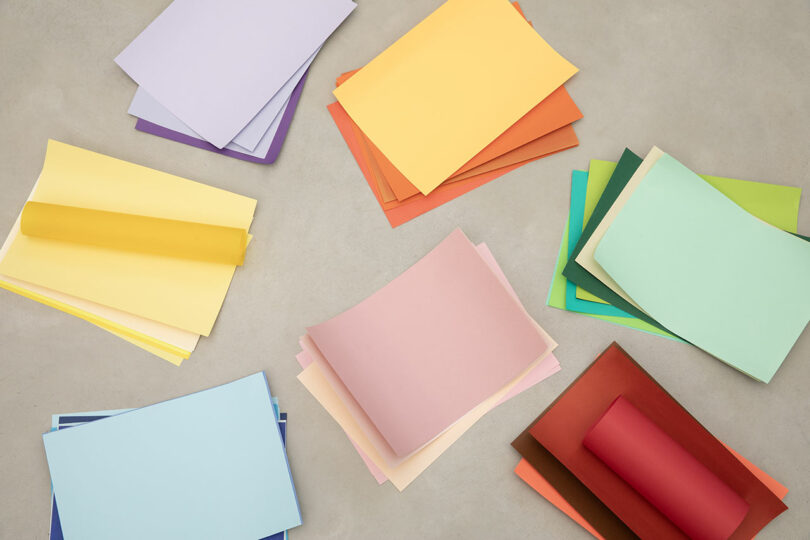 Stacks of colored paper in various pastel and bright shades arranged in clusters on a plain light surface.