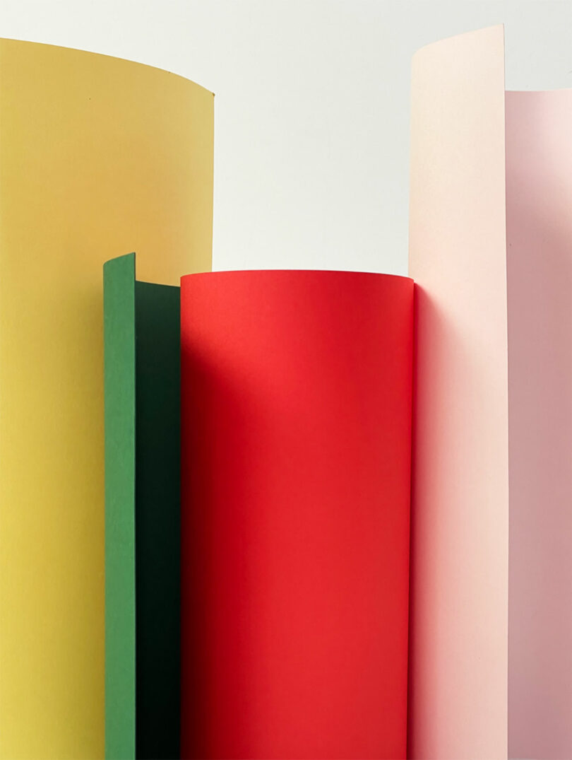 Several sheets of colored paper—yellow, green, red, and light pink—are standing upright against a plain white background.