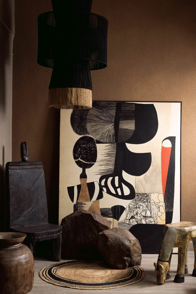 A room featuring abstract black and white artwork, rustic wooden and stone furniture, a woven mat, and a black pendant light with fringe.