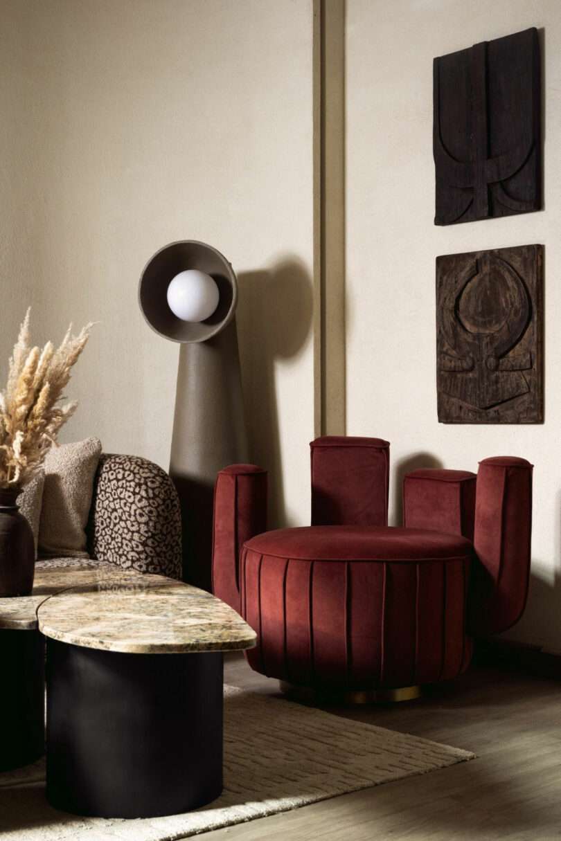 A modern living room with a red velvet accent chair, a marble coffee table, a sculptural floor lamp, and abstract wall art on a neutral-toned wall.
